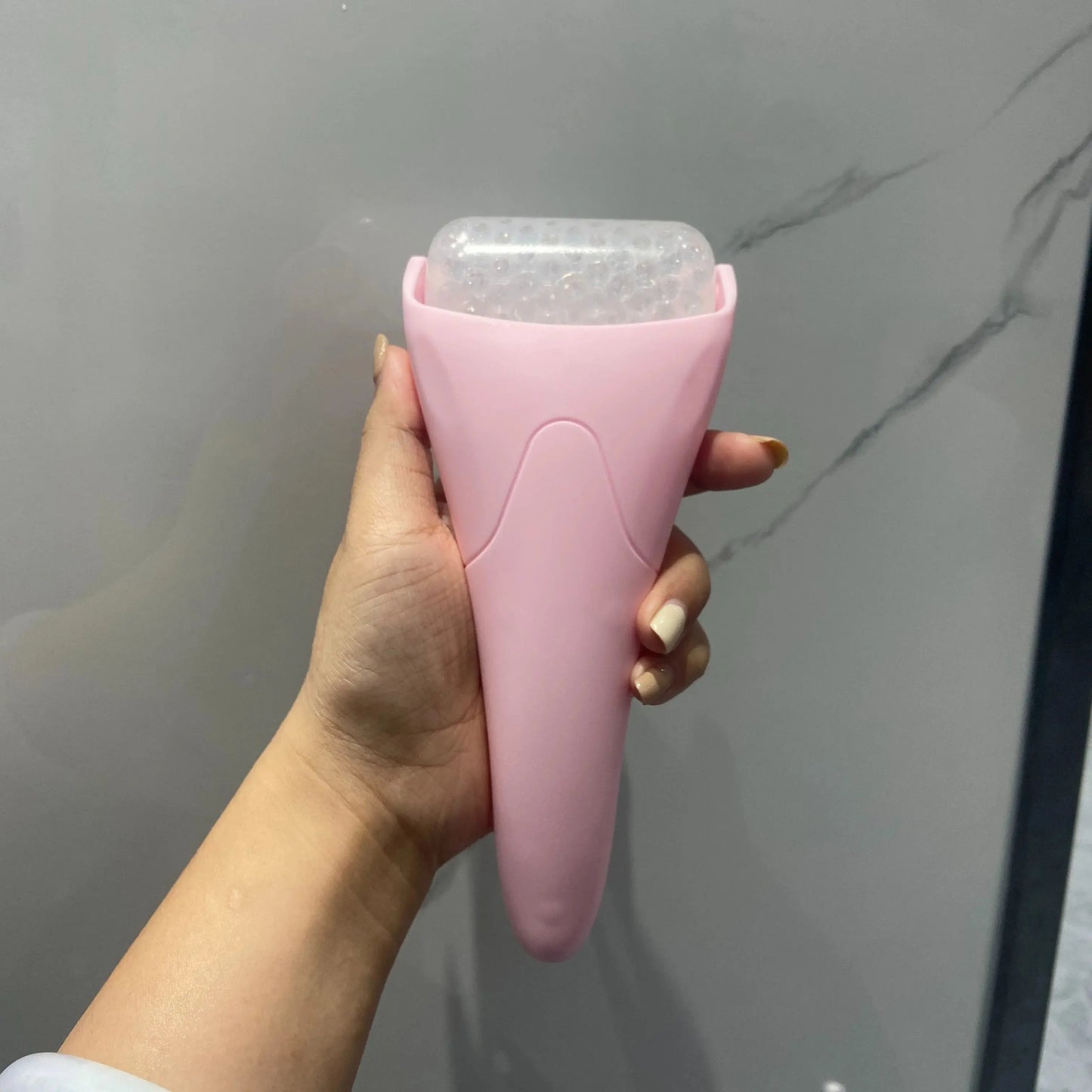 Handheld facial ice roller massager tool in pink, with clear ice cylinder head