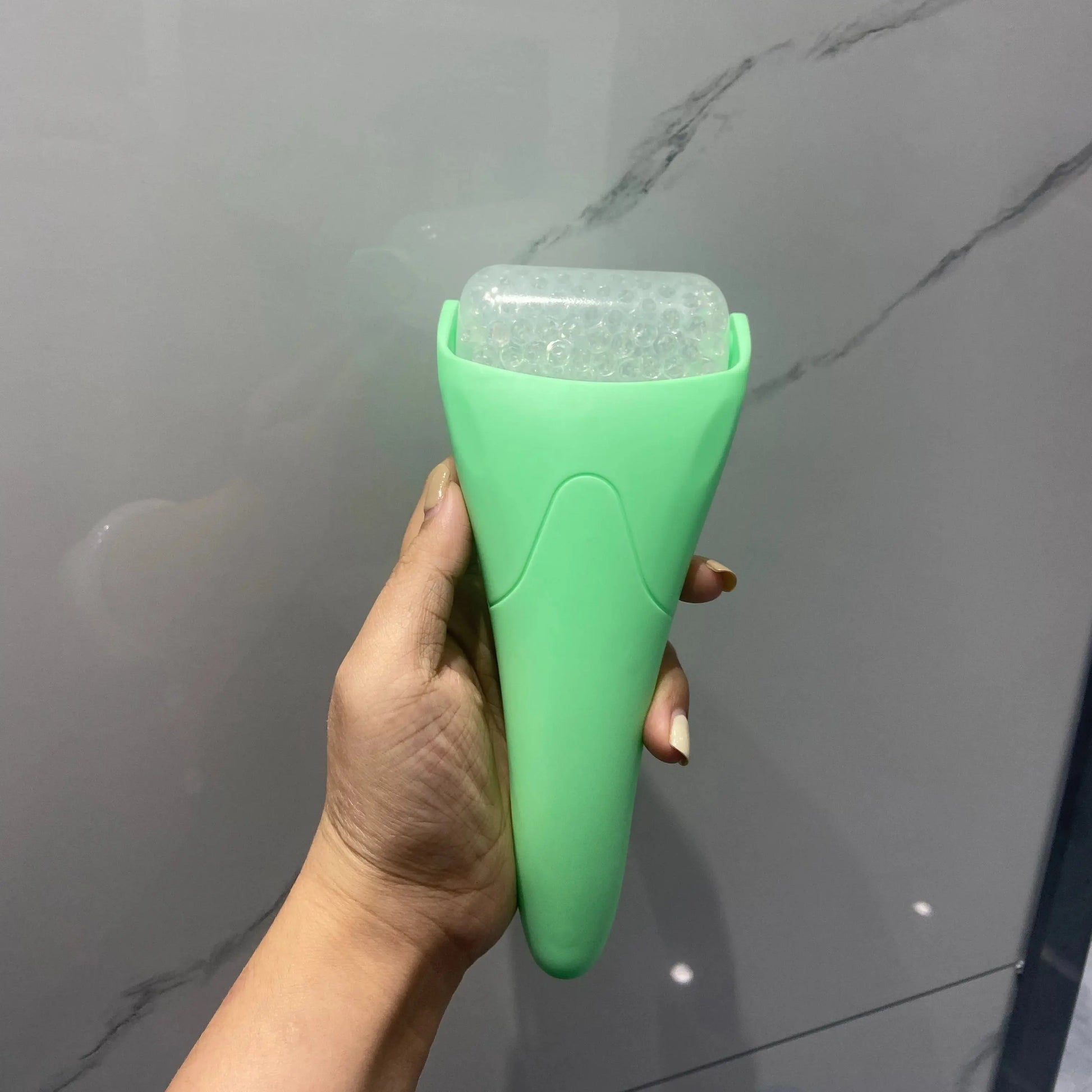 Handheld facial ice roller massager tool in green, with clear ice cylinder head