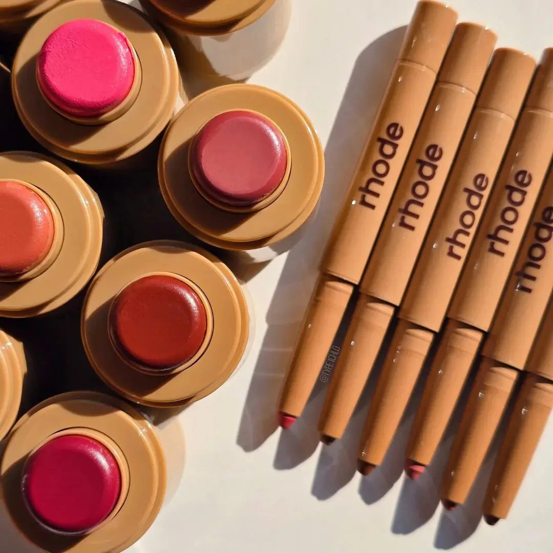 Assorted lip glaze tins and tubes, including pink and nude shades with caps on