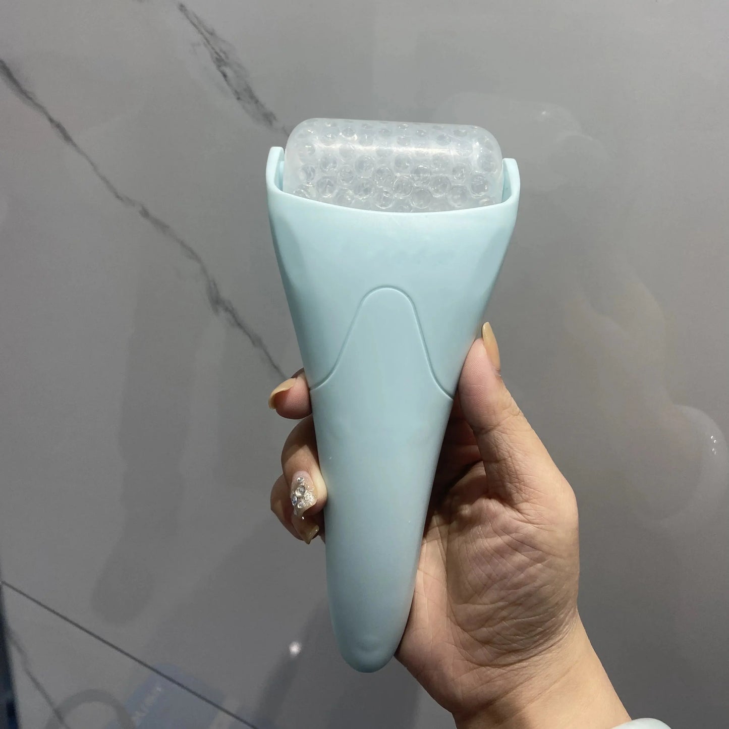 Handheld facial ice roller massager tool in light blue, with clear ice cylinder head
