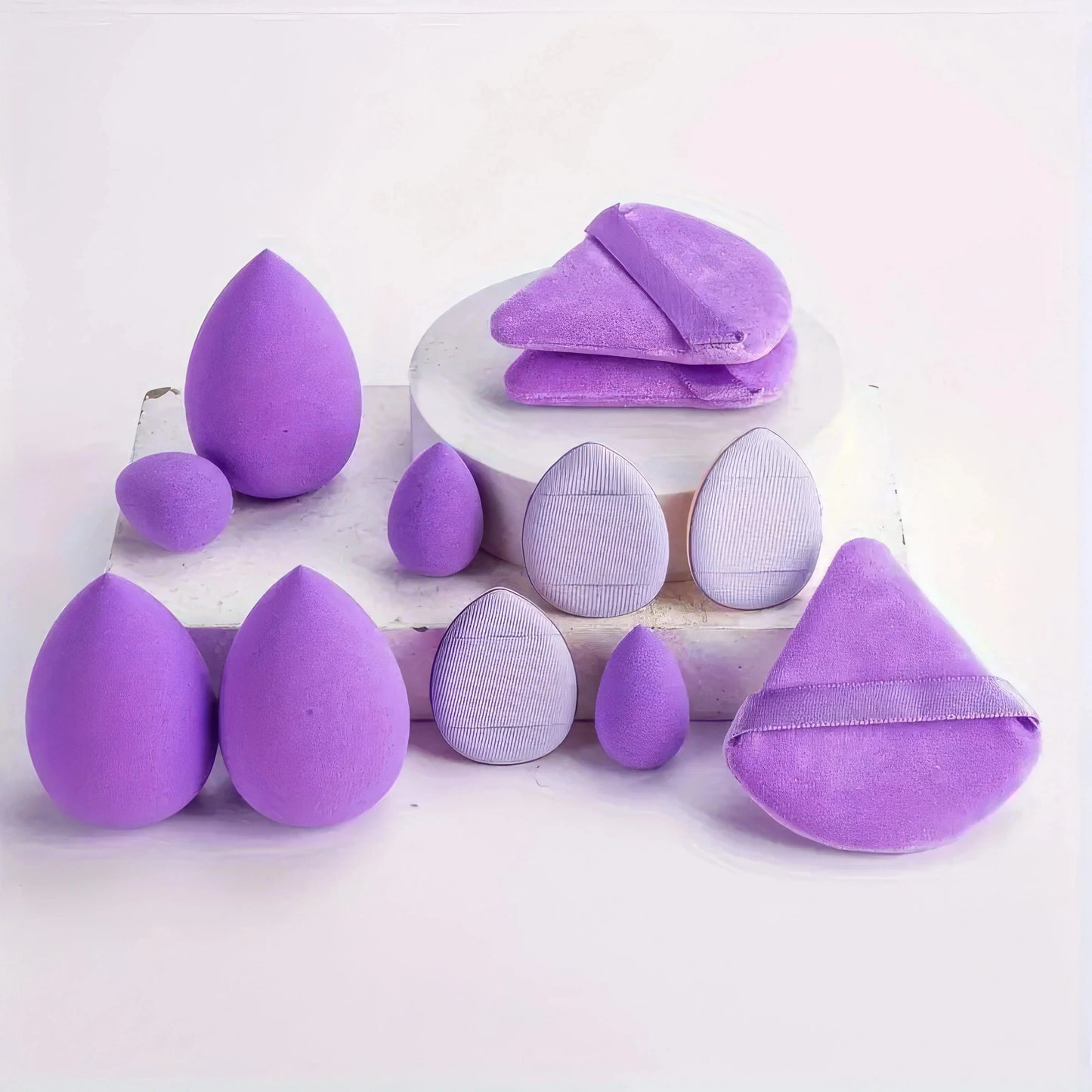 Purple and lavender egg makeup sponges set on a white plate, assorted shapes.