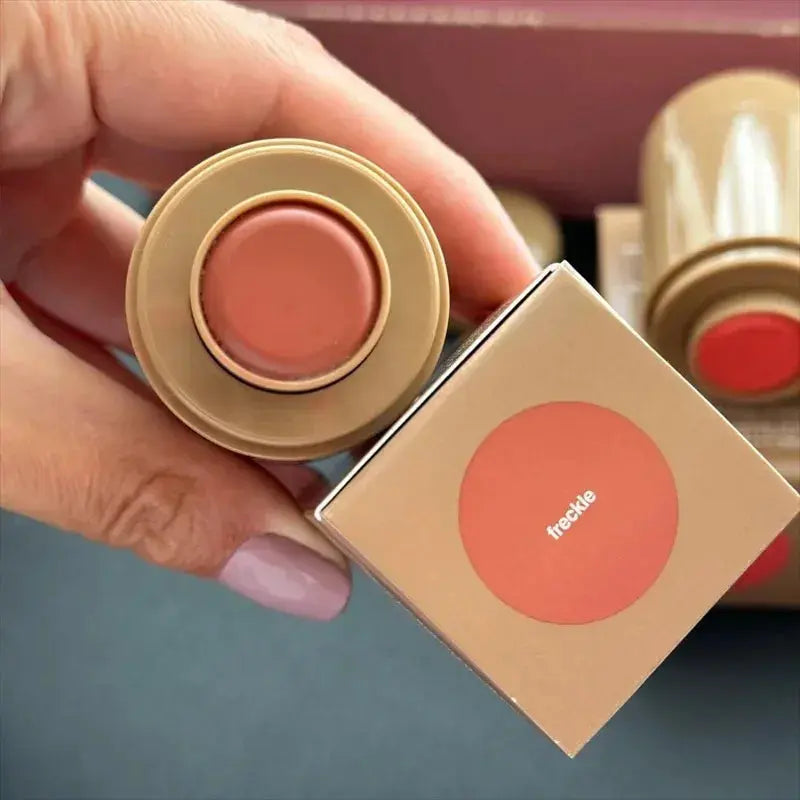 Lip glaze tins in warm peachy tones with circular labels; one open lid shown